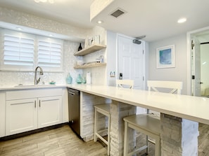Modern kitchen with sleek white finishes, bar seating, and open shelving for a clean, airy vibe.
