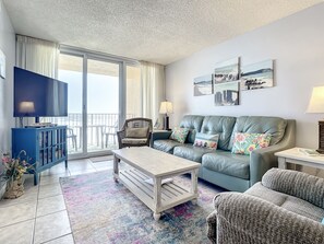 The spacious living area boasts comfortable seating, vibrant decor, and sliding doors leading to the balcony, blending indoor and outdoor relaxation.