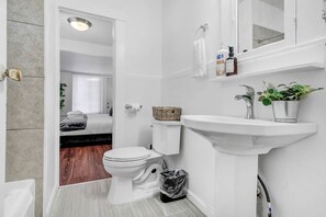 Indulge in a serene bathroom escape, showcasing a rejuvenating handheld shower, a calming bathtub, and an assortment of exclusive toiletries for your pampering.