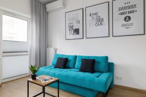 A vibrant living area with a bright turquoise sofa, minimalist black-framed artwork, and a small coffee table, adding a contemporary touch.

