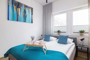 A cozy bedroom with a turquoise and white color scheme, a soft bedspread, and large windows allowing natural light to flood the space.

