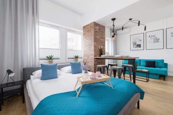A stylish and modern bedroom featuring a turquoise bedspread, exposed brick accents, and sleek black pendant lights, creating a bold and cozy atmosphere.

