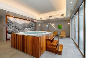 A luxurious spa section with a sizable wooden hot tub, atmospheric lighting, and a nature-inspired wall mural adding a tranquil vibe.