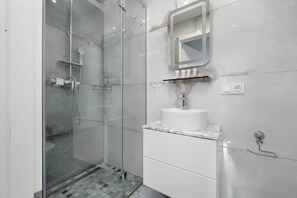 A modern bathroom with a glass-enclosed shower, marble-patterned tiles, and sleek fixtures.
