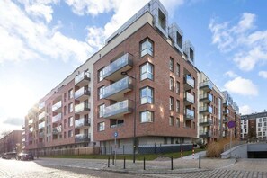The exterior of a contemporary red-brick apartment complex with large balconies and a pedestrian walkway.
