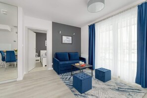 A cozy living area with a blue sofa, matching curtains, and a bright open layout leading to the kitchen.

