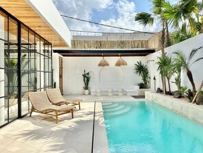 Outdoor area with a shaded lounge, two daybeds, shower, and a swimming pool