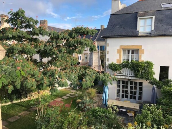 Vue de la maison, côté village, au printemps et en été, avec le jardin. 