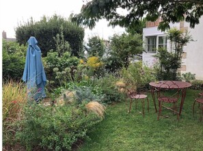 Vue du jardin devant la maison, avec la table en fer forgé sous l'arbre. 