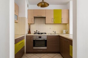 A functional kitchen with a mix of wooden and green cabinets, a built-in oven, and stylish lighting, offering a practical cooking area.

