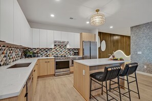 The fully equipped modern kitchen features culinary essentials, stainless steel appliances, and island bar seating.