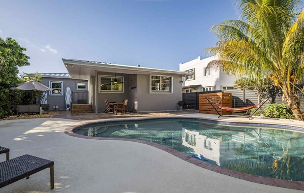 Expansive backyard oasis featuring a pool, abundant outdoor seating, and lush tropical foliage for an authentic island ambiance.