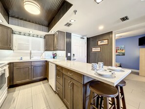 Enjoy cooking in this stylish kitchen with sleek cabinetry, a spacious breakfast bar, and contemporary lighting, creating a perfect blend of function and beachside charm.