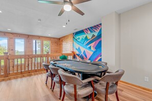 A plush poker table set against a vibrant geometric mountain mural and framed by large wooden windows