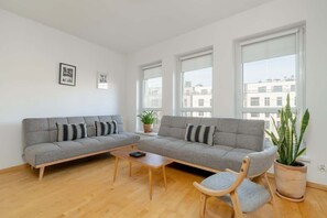 Another angle of the living room, highlighting the large windows, gray L-shaped sofa, and minimalist decor for a modern aesthetic.

