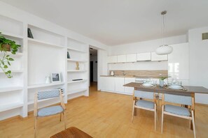 An open-plan living and dining area with white cabinetry, wooden flooring, and a stylish dining set, combining functionality with elegance.

