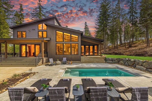 Evening Oasis With Illuminated Poolside, Tiered Lounge Seating + Full-Glass Windows Showcasing Interior Warmth