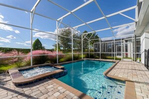 Relax in your private oasis with a sparkling pool and hot tub, surrounded by lush greenery and under a clear blue sky.