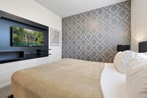 Rest in luxury with a plush queen bed against a classic damask wall, complete with a sleek TV for downtime entertainment.