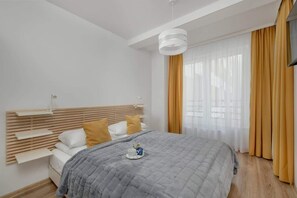 A stylish bedroom with a wooden headboard, soft gray bedding, and floor-to-ceiling mustard curtains, creating a cozy and warm atmosphere.

