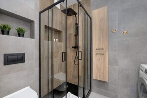 A contemporary bathroom with dark gray tiles, a glass-enclosed shower, and a modern black showerhead, adding a luxurious feel.

