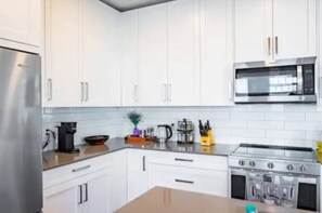 This modern kitchen features white cabinetry, stainless steel appliances, and light grey countertops. A subway tile backsplash enhances the bright, clean look, while a large window fills the space with natural light. A small plant adds a cozy touch.