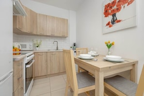 A compact kitchen with wooden cabinets, a dining table set for two, and a white backsplash, offering a warm and functional cooking space.


