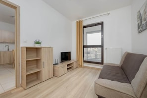 A bright living area with a brown sofa, a wooden TV stand, and a floor-to-ceiling window allowing natural light to enhance the space.

