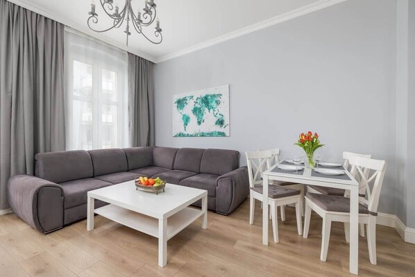 A stylish living and dining area with a gray sofa, a white coffee table, and a dining set, complemented by modern wall art and a chandelier.

