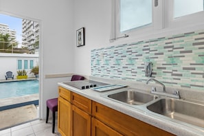 Fully stocked kitchen with a view of the pool. Stainless steel appliances, including a refrigerator and oven, along with ample counter space and modern cabinets. Large window brings in natural light and highlights the pool area.