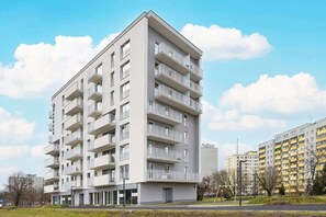 An exterior shot of the contemporary apartment building, featuring a sleek design, large balconies, and a surrounding urban skyline.

