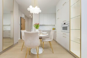 A modern dining area with a round table, velvet chairs, and golden accents, seamlessly blending with the kitchen space in an open-concept layout.

