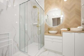 A stylish bathroom with marble-style tiles, a walk-in shower with a glass partition, and a wooden accent wall for a warm, sophisticated look.

