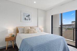 Find calm and relaxation in the comfortable queen-sized bedroom with light and warmth streaming in from the balcony.

