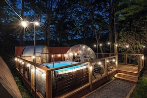 Night time exterior view of the hot tub and dome surrounded by string lights.