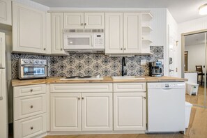 Kitchen with stovetop, toaster oven, fridge, dishwasher, blender & drip coffee maker.