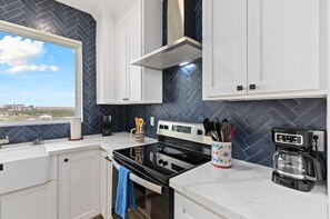 Unit 201 Kitchen:
Take in the serene views just outside the window as you prepare meals in the chef-inspired kitchen. Enjoy a warm cup of coffee or tea at the quartz-topped island, fully stocked with all the essentials. This sleek and modern space features stainless steel appliances, a stylish tile backsplash, custom cabinetry with built-in trash bins, and a convenient spice ra...