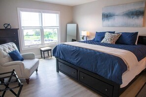 A luxurious king bed, adorned with crisp, inviting linens, anchors the room beneath a captivating painting. The full-size mirror allows you to do a thorough fit check before heading out for the day. A dresser provides storage, while a single plush ch