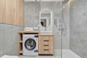 A compact yet functional bathroom featuring a washing machine, a walk-in shower with glass partitions, and wooden storage cabinets for a stylish finish.

