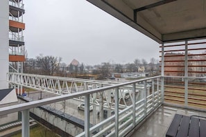 A balcony view overlooking the city, featuring a metal railing and a wooden floor, providing an inviting outdoor space.

