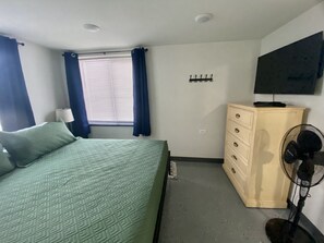 King bed with tv, dresser, blackout curtains, fan, and some hangers. 
