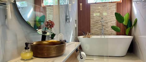 Step into a private spa retreat featuring a soaking tub, rain shower, and gold vessel sink. Surrounded by natural textures and tropical greenery, this serene space blends elegance and comfort with every detail designed for relaxation