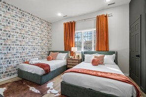 Relax in this stylish room featuring twin beds adorned with plush pillows and soft linens. You'll love the vibrant wallpaper and natural light that pours in from the large window, creating a cozy and inviting atmosphere.