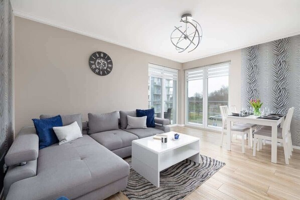 A stylish living room with a gray L-shaped sofa, blue accent pillows, a modern coffee table, and a TV mounted on the wall.

