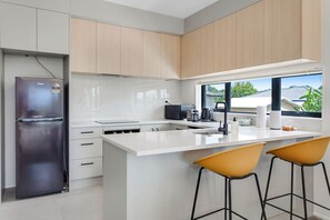 The modern white kitchen has pops of colour with the yellow bar stools and black accessories.