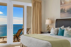 Elegant master bedroom featuring a king-size bed, serene coastal décor, and private balcony access with stunning ocean views