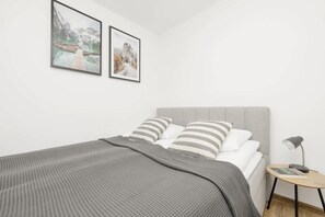 A modern bedroom featuring a comfortable bed with striped bedding, a wooden bedside table, and minimalist decor.

