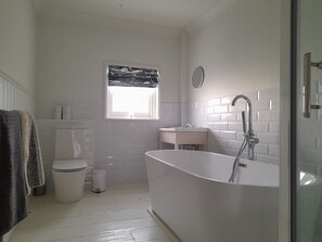 The top floor bathroom has a large feature bath, separate shower, toilet, basin and towel rail.