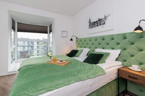 A bright bedroom with a luxurious green upholstered headboard, neatly arranged pillows, and a comfortable bed with soft linens.

