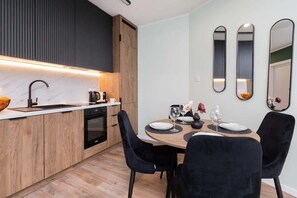 A modern open kitchen with black and wooden cabinets, pendant lighting, and a seamless connection to the dining area.

